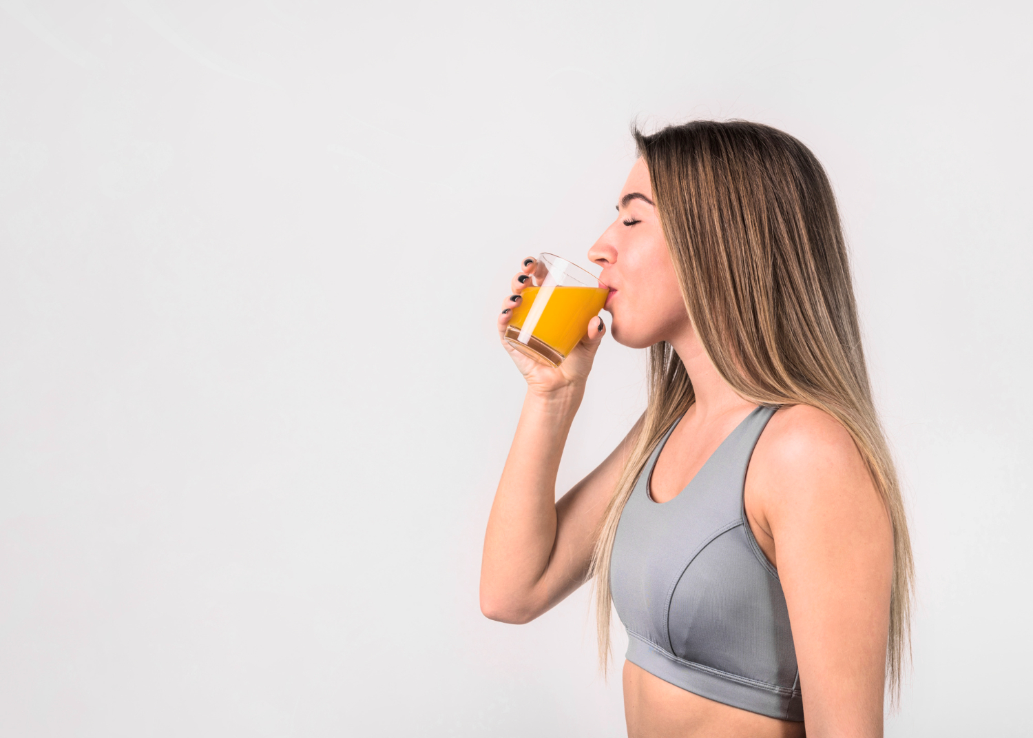 Mulher jovem vestindo roupa esportiva bebendo um copo de suco natural, simbolizando o cuidado com a hidratação e o bem-estar após a prática de exercícios físicos.
