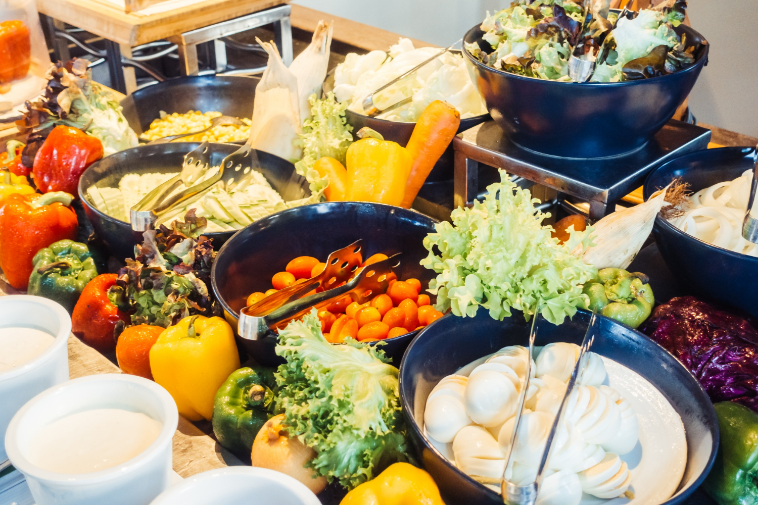 Buffet de vegetais colorido com diferentes tipos de saladas, legumes frescos, ovos cozidos e molhos, disposto em tigelas sobre uma mesa de restaurante.