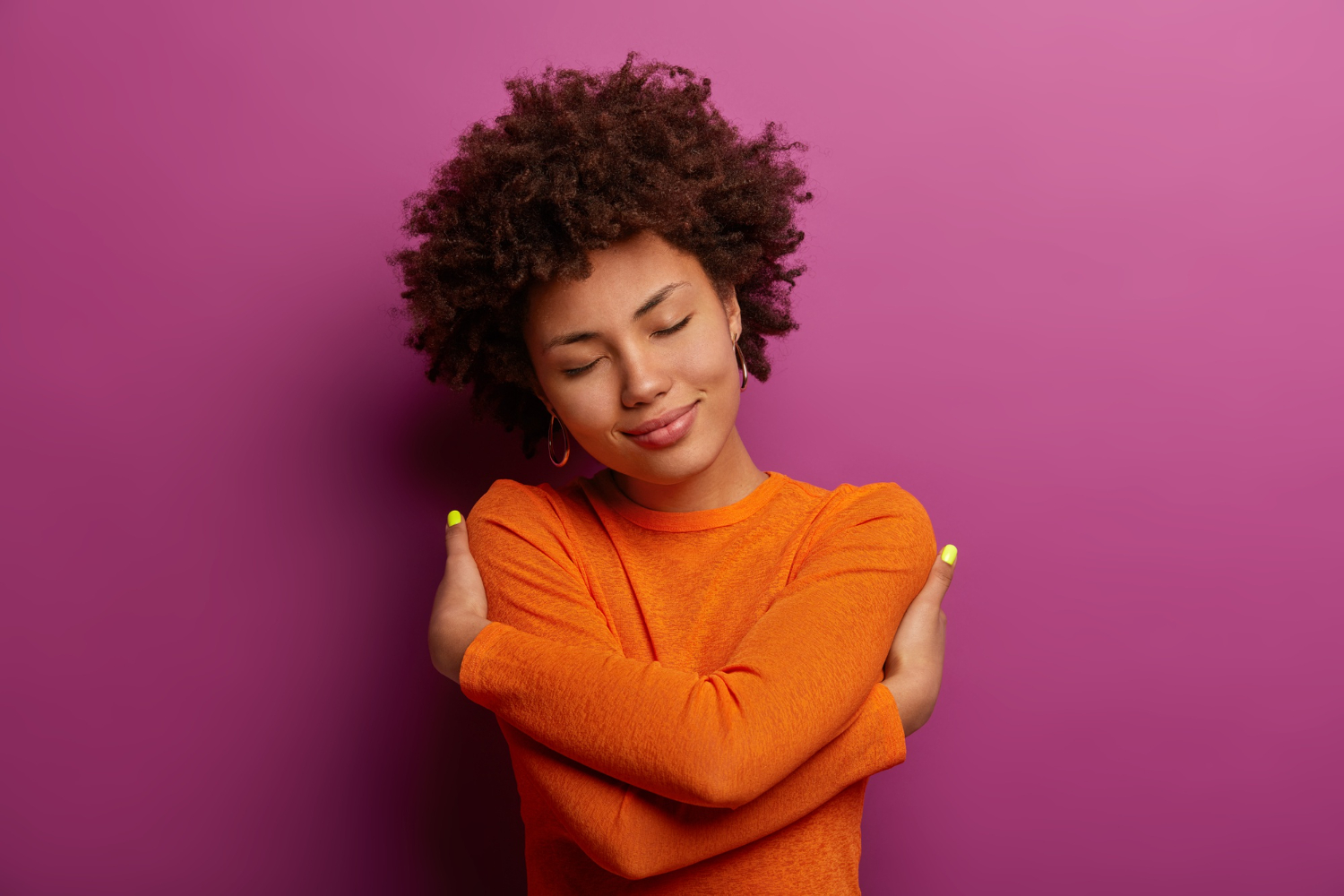 Mulher de olhos fechados e expressão serena se abraça, simbolizando amor-próprio e a importância de cuidar da saúde mental.