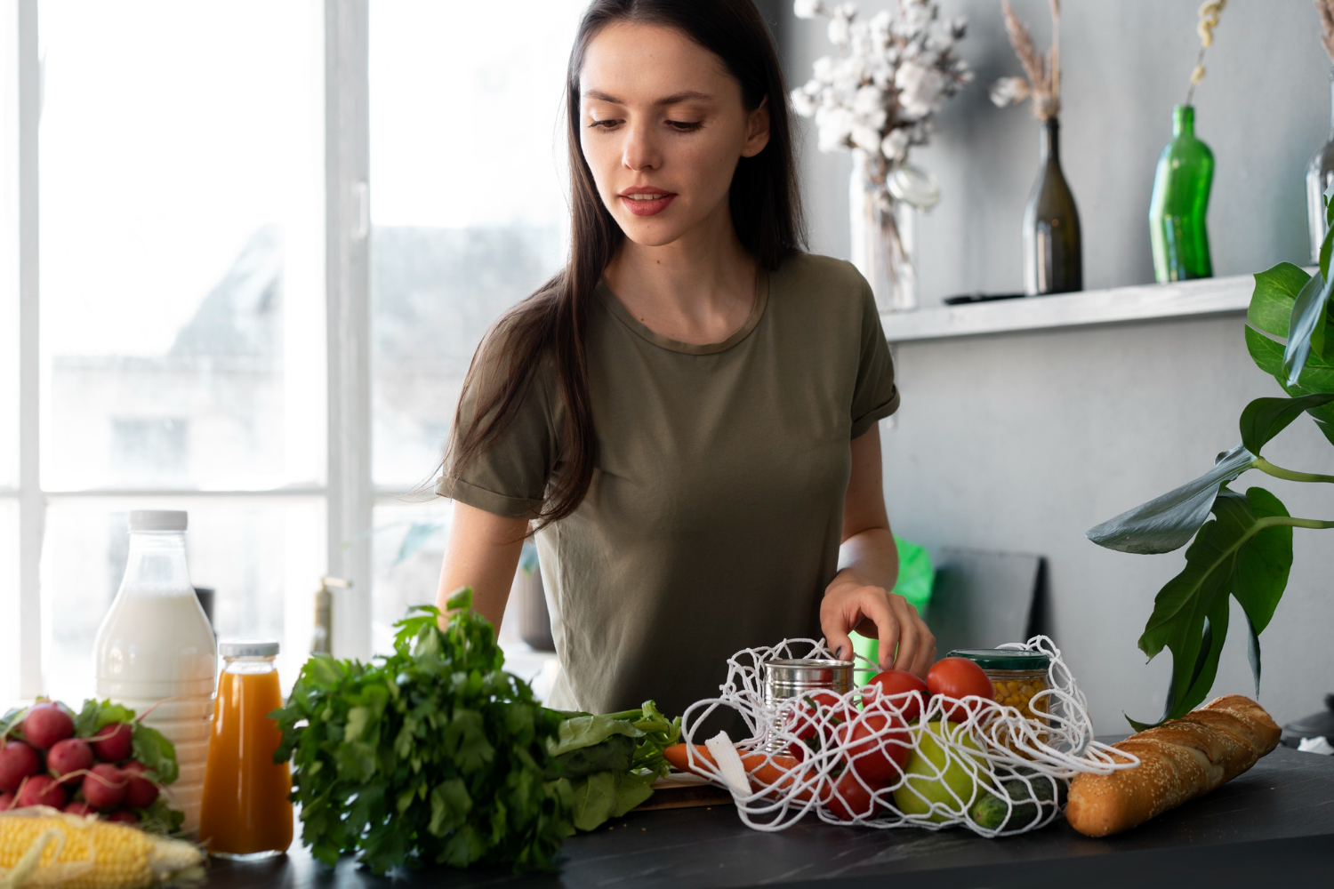 Mulher organizando alimentos frescos como vegetais, frutas, pão e leite sobre a mesa, simbolizando o início de uma rotina de alimentação saudável.